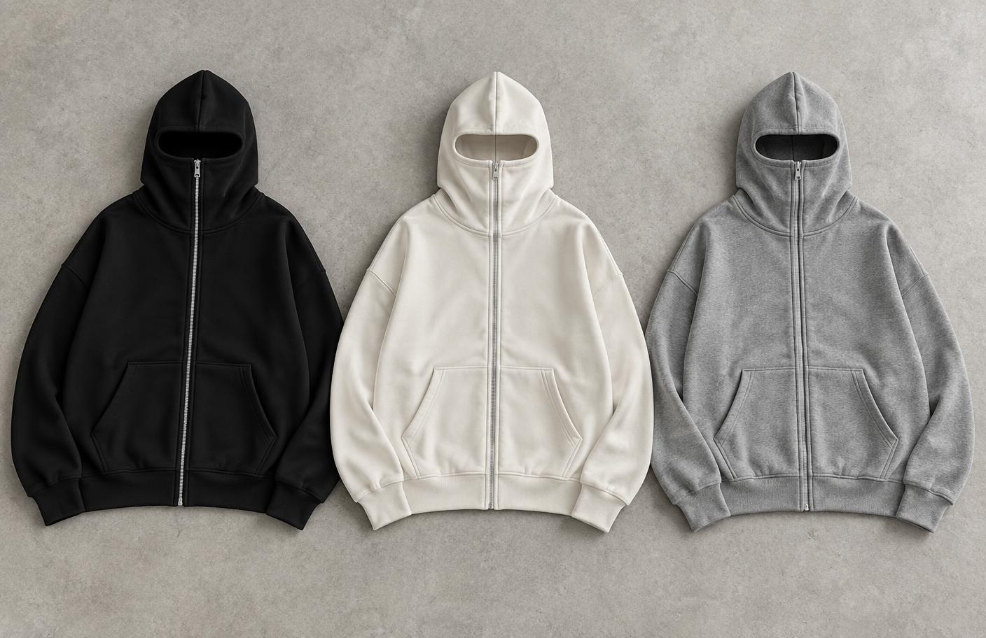 Three oversized zip-up hoodies with built-in face masks laid flat side by side in black, off-white and heather grey